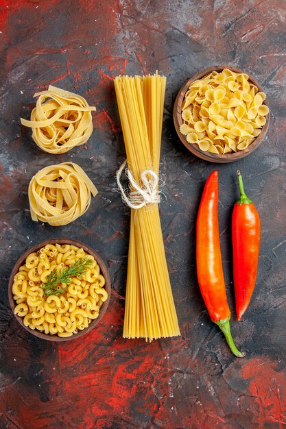 Free photo vertical view of various types of uncooked pastas and peppers on mixed color background