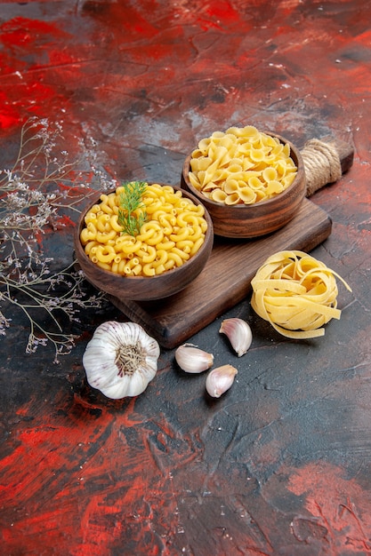 Foto gratuita vista verticale di vari tipi di pasta cruda sul tagliere di legno e aglio su sfondo di colore misto