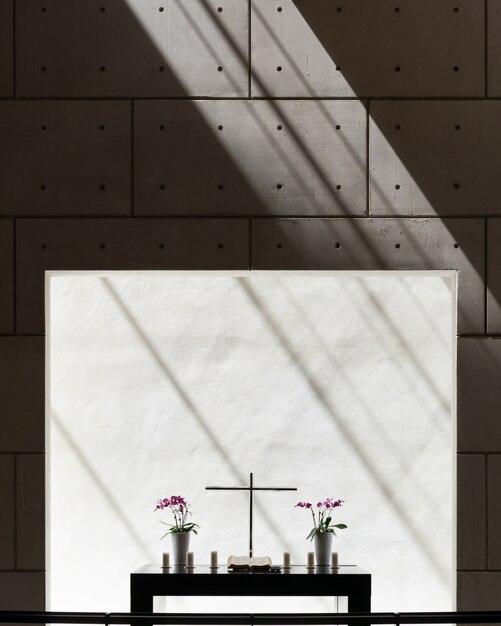 Вертикальный вид на вазы и крест на столе в комнате с бетонной стеной
