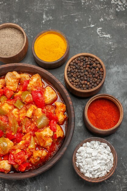 Vertical view of vegetable spicy chicken soup in a brown pot and different spices