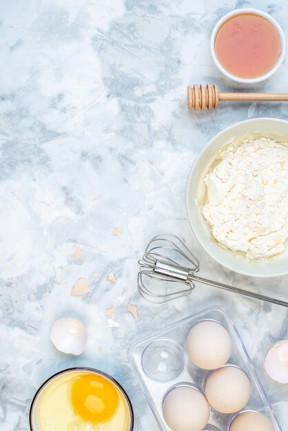 Vertical view of white flour in a bowl and stainless cooking tool eggs jam on the left side on two-toned background