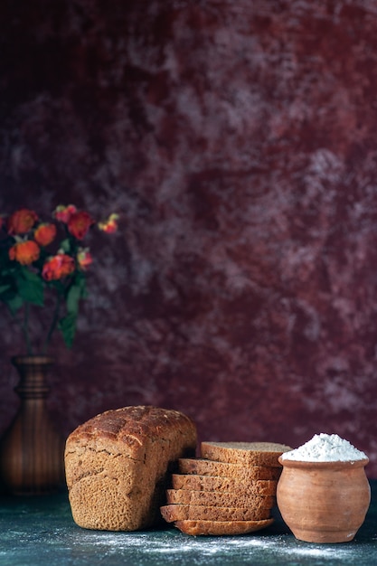 Vertical view of whole cut dietary black bread and flour in bowl flower pot on blue maroon colors background