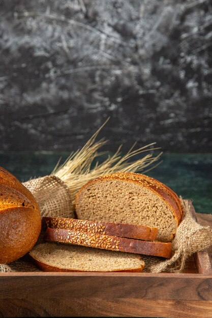 Vertical view of whole and cut fresh black bread in a brown wooden box on dark colors surface