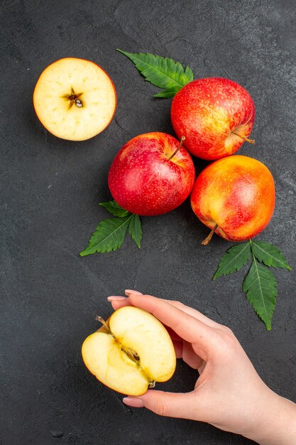 Vertical view of whole and cut fresh red apples and leaves on black background