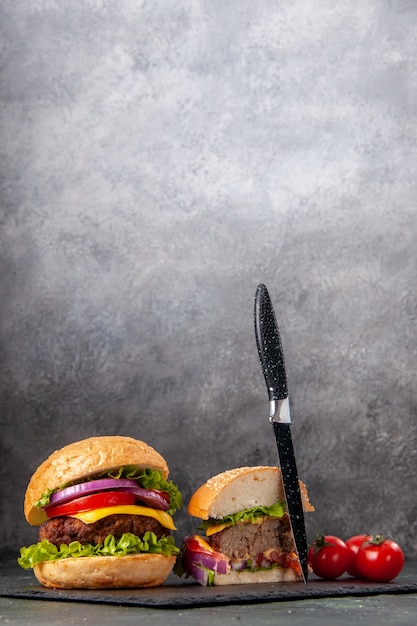 Vertical view of whole cut tasty sandwiches and tomatoes with stem knife on black tray on dark mix color surface