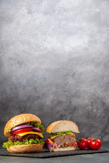 Free photo vertical view of whole cut various tasty sandwiches and tomatoes with stem on black tray on gray blurred surface