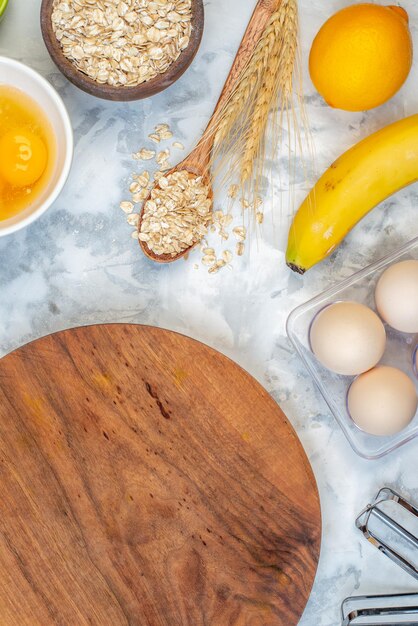 Vertical view of wooden round board and ingredients for the healthy food set on stained white table