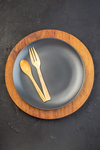 Vertical view of wooden spoon and fork on black on brown plates on dark color surface