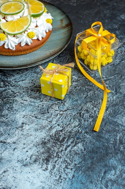 暗いテーブルにレモンで飾られた美しい黄色のギフトボックスとケーキとクリスマスの背景の垂直方向のビュー