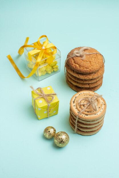파스텔 녹색 배경의 장식 액세서리 옆에 쌓인 다양한 맛있는 쿠키와 아름다운 노란색 선물 상자가 있는 xsmas 분위기의 수직 보기