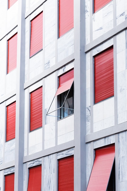 Вертикаль белого здания с окнами с красными жалюзи