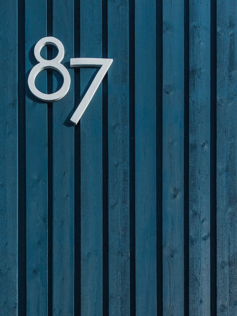 Vertical of a wooden blue wall with vertically arranged sticks and white number eighty-seven
