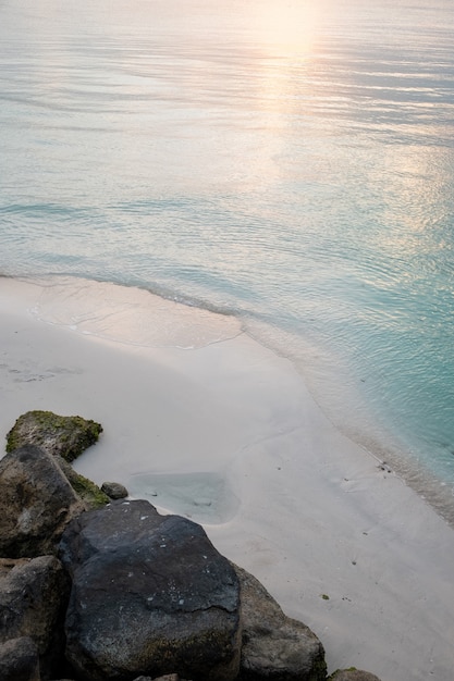 Verticals shot of a sandy beach with the reflection of the sun in the blue water