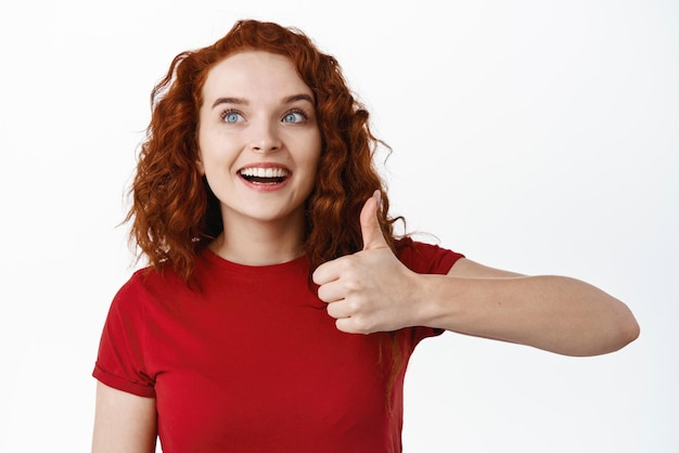 Free photo very good awesome excited ginger girl with pale skin looking amazed at logo banner and show thumb up in approval like something good praise advertisement white background