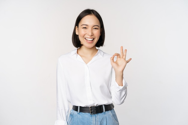 Very good Smiling asian woman showing okay with satisfied face expression praise and compliment great job pleased by smth standing over white background