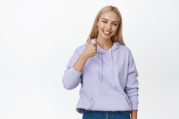 Very good Smiling blond woman showing thumbs up in approval give positive feedback like gesture standing over white background