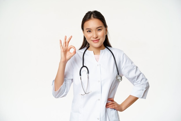 Very good smiling confident asian female doctor showing okay ok sign in approval confirm smth saying...
