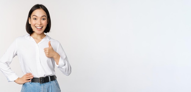 Very good Smiling enthusiastic asian female entrepreneur showing thumb up in approval praise excellent job satisfied with results standing over white background