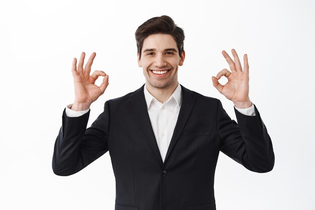 Very good. Smiling satisfied businessman, male entrepreneur in business suit, show okay signs and nod in approval, say yes, agree and praise work, white background