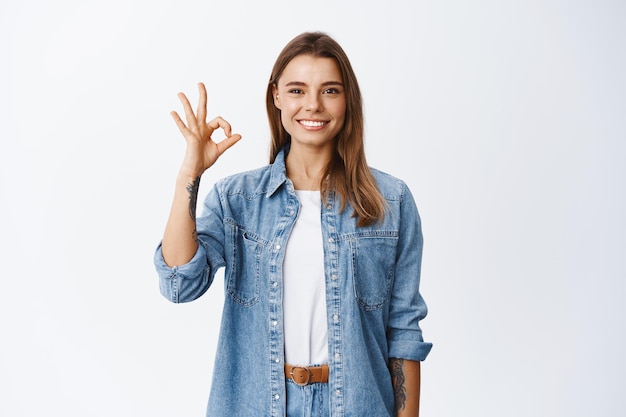 Very good. Smiling young blond woman showing okay sign and looking satisfied, approve good thing, standing satisfied on white, praise product