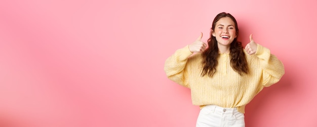 Free photo very good well done smiling girl being supportive laughing and showing thumbs up in approval like awesome idea praise you standing against pink background