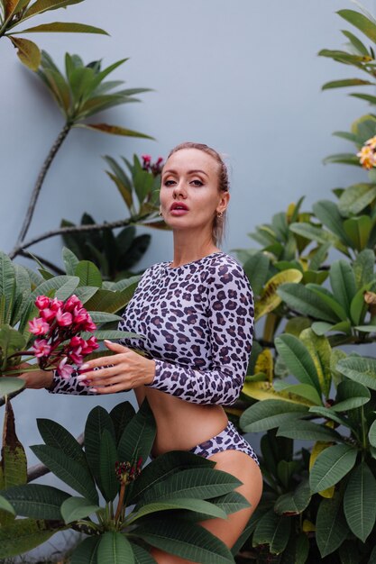 Very pretty caucasian woman with perfect fit body in leopard swimsuit with tropical beautiful flowers