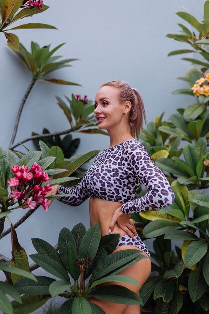 Very pretty caucasian woman with perfect fit body in leopard swimsuit with tropical beautiful flowers