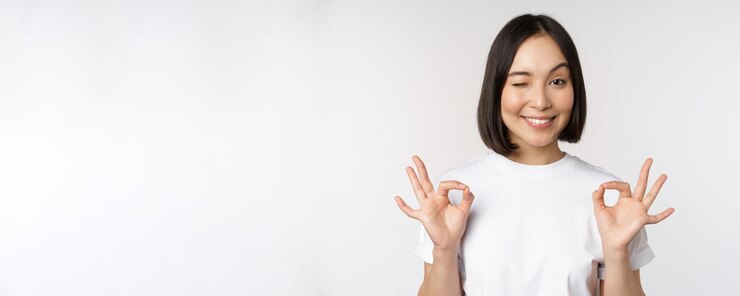 無料Photo 非常に優れた笑顔のアジアの女性は、白い背景の上に立っているsmthを推奨して満足しているように見える大丈夫なサイン承認を示しています