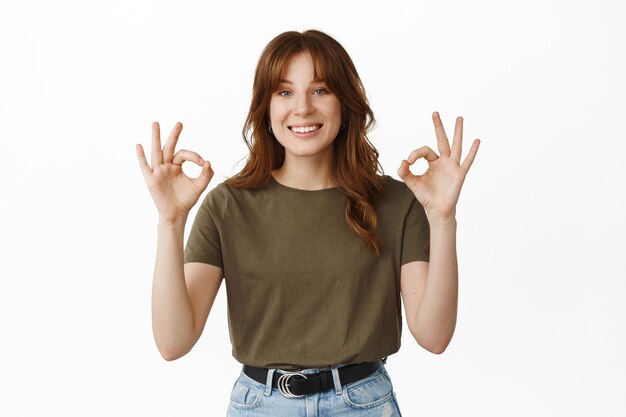 Very well, good job. Smiling young woman showing Okay ok gesture, nod in approval, say yes, agree with your choice, praise great thing, standing on white