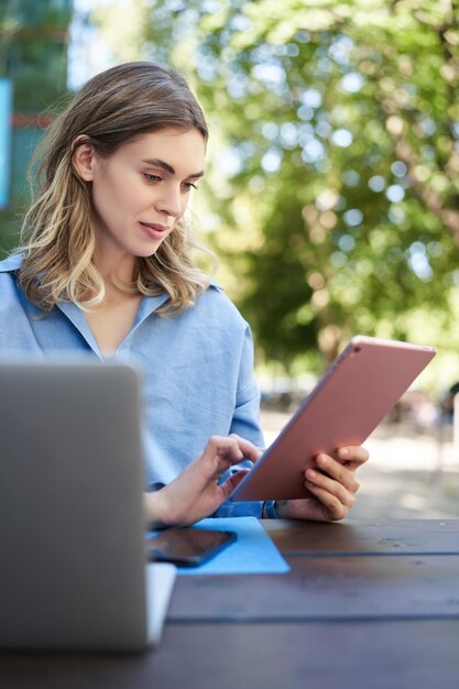 屋外で勉強しているデジタル タブレットで読んでいる若い女子学生の垂直方向のショット実業家シッティ