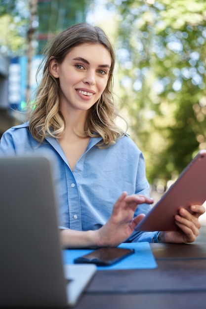 Colpo vetical di giovane studentessa che legge sulla tavoletta digitale che studia all'aperto donna d'affari sitti