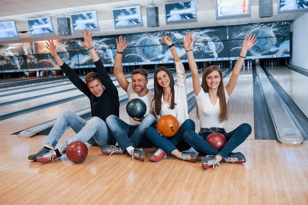 Victory position. Young cheerful friends have fun in bowling club at their weekends