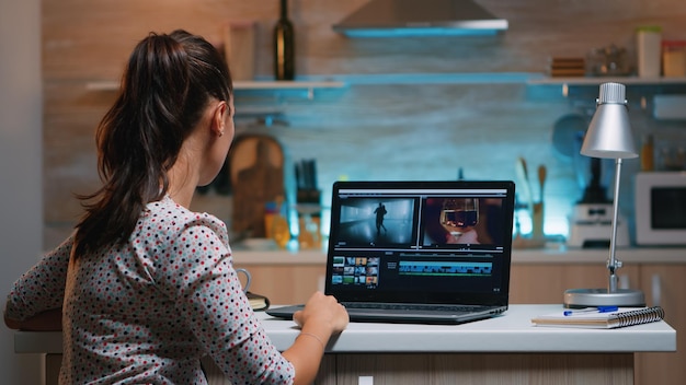 Editor video che lavora da casa di notte al nuovo progetto di montaggio di film audio seduto in cucina moderna. creatore di contenuti che utilizza una rete wireless di tecnologia moderna per laptop professionale