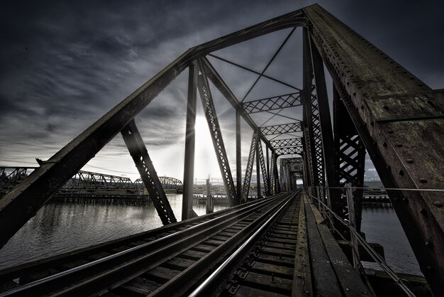 湖の近くの線路と暗い空に輝く息をのむような太陽が輝くVierendeel橋
