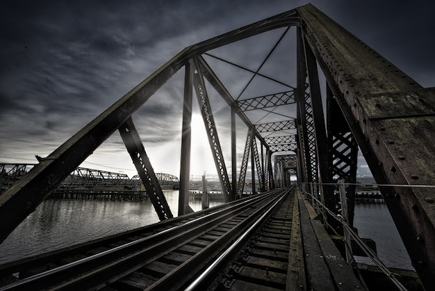 Vierendeel bridge with train track near the lake and the breathtaking sun shining in the dark sky