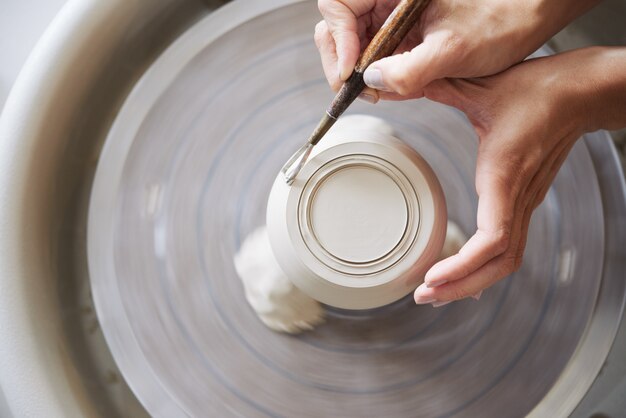 Above view of anonymous hands carving a pot from clay