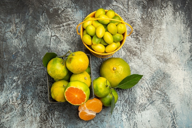 Above view of a basket and bucket full of fresh green tangerines cut in half and peeled tangerine on gray background