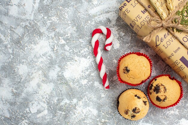 Above view of beautiful Christmas packed gift with love inscription and small cupcakes on ice surface