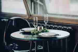 Free photo view over beautifully decorated round table with natural fir branch, candle, two flutes, plates against classic sofa in modern apartment.