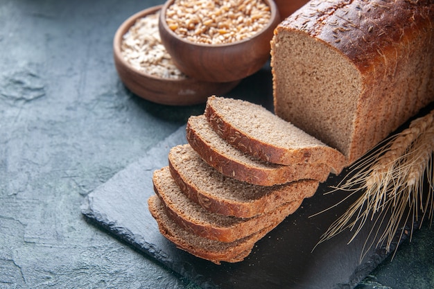 Above view of black bread slices flour oatmeal buckwheat on dark color board on blue distressed background