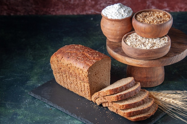 Above view of black bread slices flour oatmeal buckwheat on dark color board on mixed color distressed background