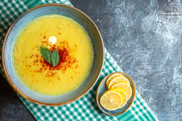 Above view of a blue pot with tasty soup served with mint and chopped lemon on half folded green stripped towel on blue background