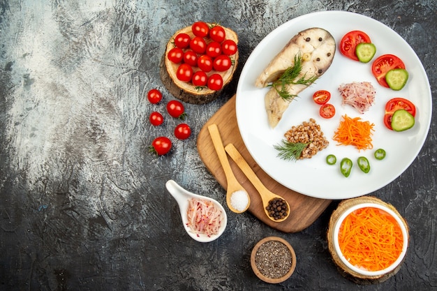 Above view of boiled fish buckwheat served with vegetables green on a white plate on wooden cutting board and spices on ice surface