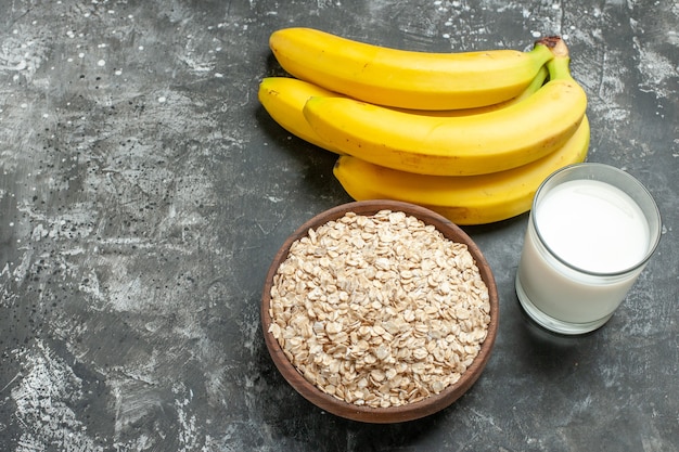 Sopra la vista dello sfondo della colazione con crusca d'avena biologica in una pentola di legno marrone latte in un fascio di banane di vetro su sfondo scuro