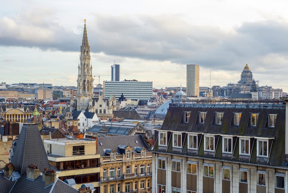 A skyline view of Brussels with the spire of the Town Hall and the Palace of Justice visible under a cloudy sky.
