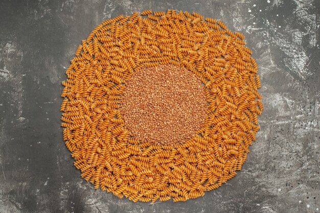 Above view of buckwheat in the middle of raw Italian pastas lined circle frame on gray background