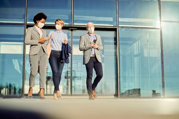 Below view of business coworkers with face masks talking while walking outdoors