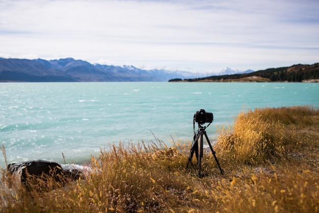 Free photo view of a camera on a stand by the beautiful lake and the hills on the horizon on a sunny day