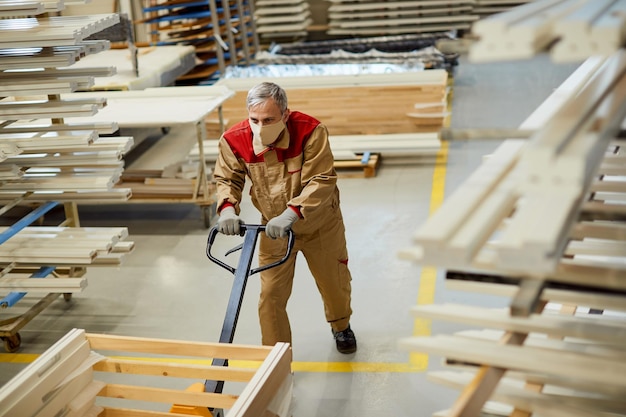 Free photo above view of carpenter with face mask pushing pallet jack in a warehouse