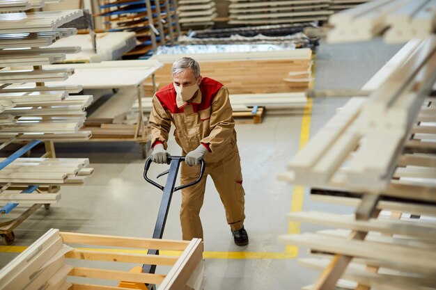 Above view of carpenter with face mask pushing pallet jack in a warehouse